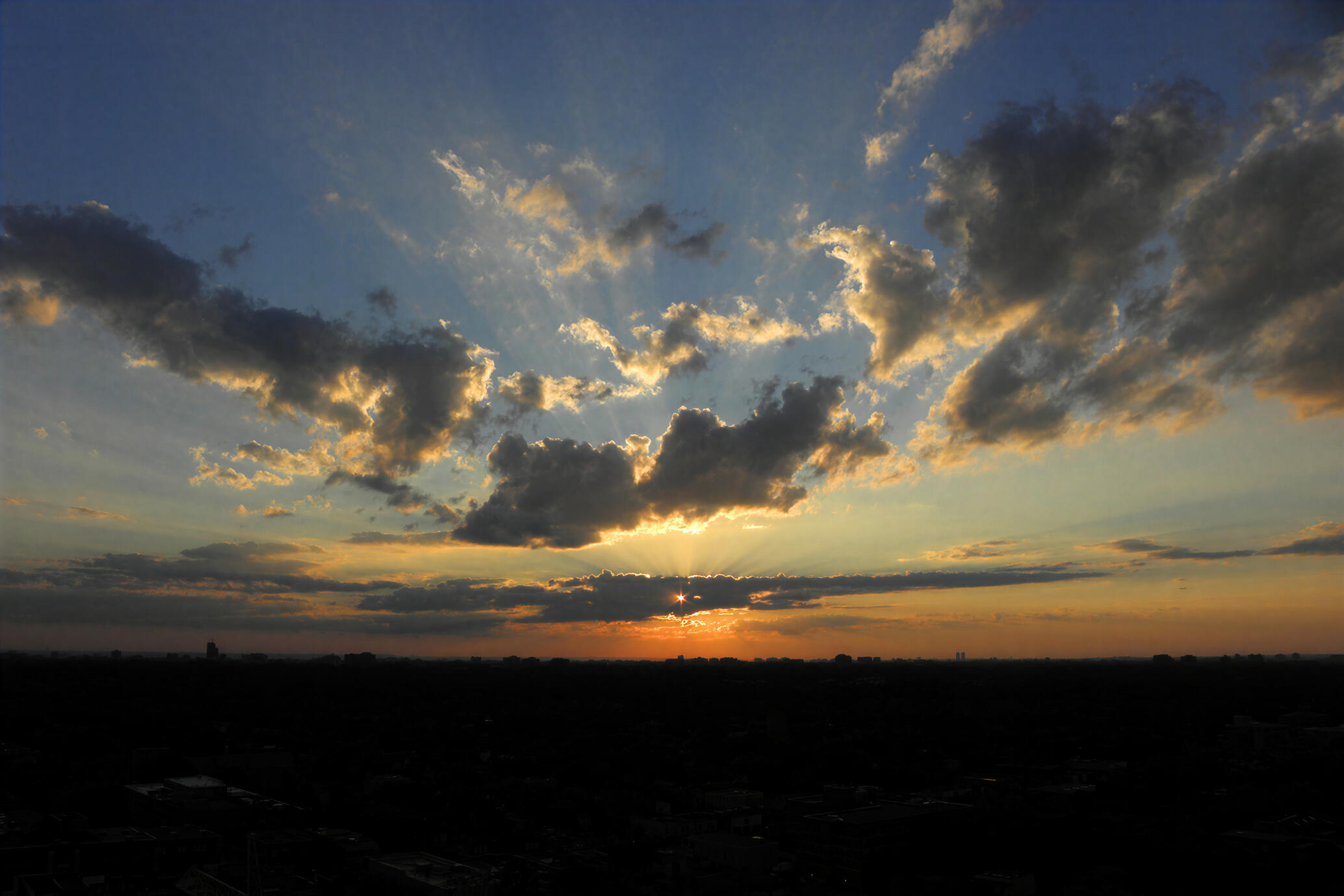 A dramatic evening sky over Toronto, where golden sunlight breaks through towering clouds as the city slowly disappears into shadow. Photographed looking west from a Toronto terrace in 2015.