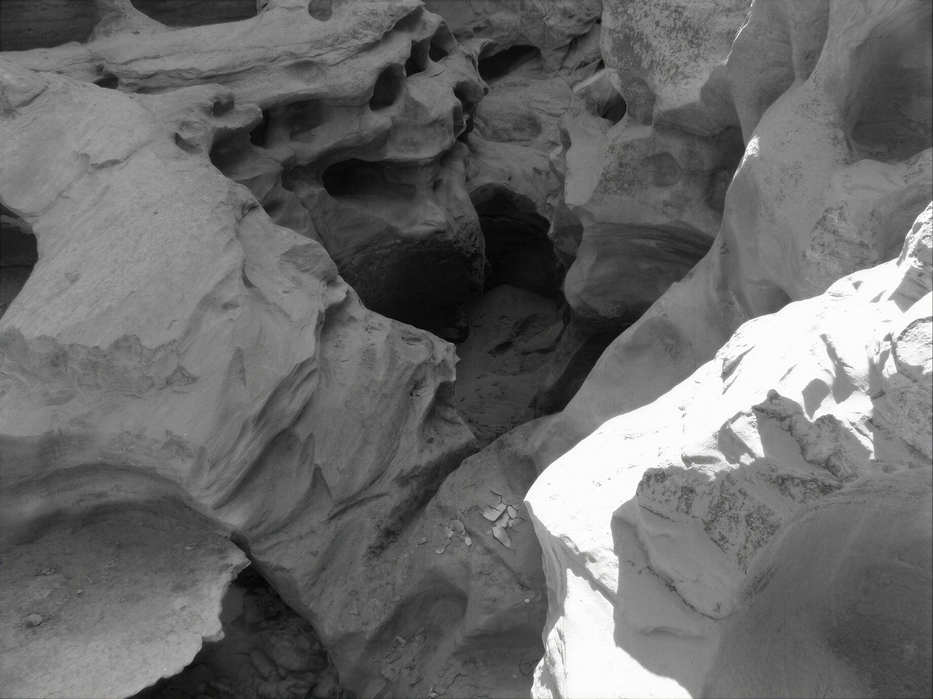 A dramatic black and white photograph of the naturally sculpted rock formations inside Chahkooh Gorge on Qeshm Island, Iran. Water erosion has created deep cavities, flowing textures and striking shadows across the ancient rock walls. Photographed in 2009.
